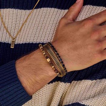 Hand med flera armband, inklusive ett guldfärgat stålarmband, mot en randig tröja.